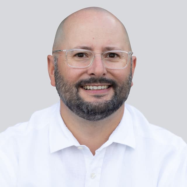 Dr. Jens Träger, lächelndes Porträt im weißen Hemd vor hellgrauem Hintergrund.